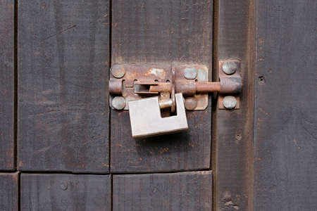 old brass lock on a rusty bolt keeping a wooden shed closed and secure from intruders and burglarsの写真素材