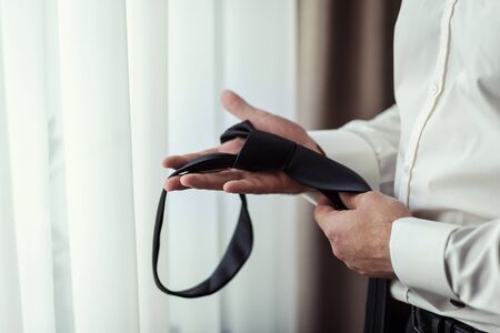 People, business, fashion and clothing concept - close up of man in shirt dressing up and adjusting tie on neck at home. Businessman putting on a tie. Man putting on necktie. Businessman getting dressed in the morningの写真素材