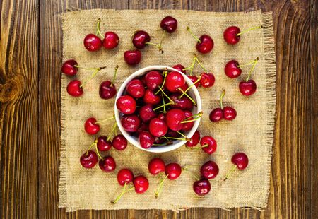 red cherries in a white ceramic bowl, red cherries on wooden table, red cherries on a brown background, bowl with cherriesの写真素材