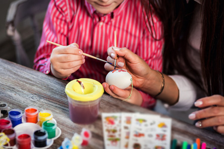 colouring eggs for eastertime at home.Happy easter! A mother and her son painting Easter eggs. Happy family preparing for Easter.decorating Easter eggs, children's hands hold a paintbrush and paintの写真素材