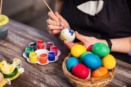 colouring eggs for eastertime at home.Happy easter! A mother,girl painting Easter eggs. Happy family preparing for Easter.decorating Easter eggs, woman hands hold a paintbrush and paintの写真素材