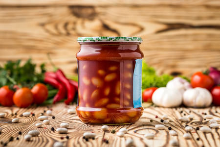 Composition of pickled beans with tomato in jar and ingredients on wooden backgroundの写真素材