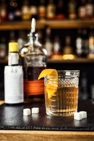 Glass of  whiskey (cognac or brandy) with lemon and ice cubes standing on the bar counter with a bottle on the backgroundの写真素材