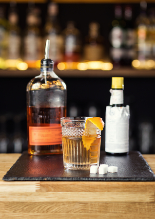 Glass of  whiskey (cognac or brandy) with lemon and ice cubes standing on the bar counter with a bottle on the backgroundの写真素材
