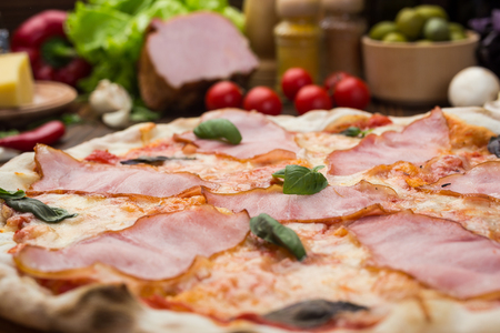 Delicious italian pizza with ham and basil leaves on wooden backgroundの写真素材