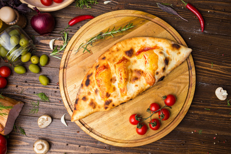 Traditional italian closed pizza Calzone with basil leaves on wooden backgroundの写真素材