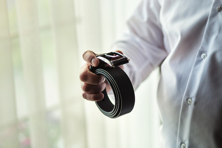 Businessman putting on a belt, fashion and clothing concept,groom getting ready in the morning...