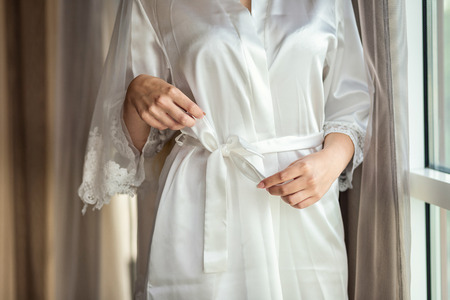 girl ties  belt on her robe standing near window,woman getting ready before wedding ceremony