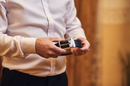 Businessman putting on a belt, fashion and clothing concept,groom getting ready in the morning before ceremonyの写真素材