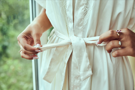 girl ties  belt on her robe standing near window,woman getting ready before wedding ceremonyの写真素材