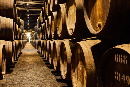 Old aged traditional wooden barrels with wine in a vault lined up in cool and dark cellar in Italy, Porto, Portugal, Franceのeditorial素材