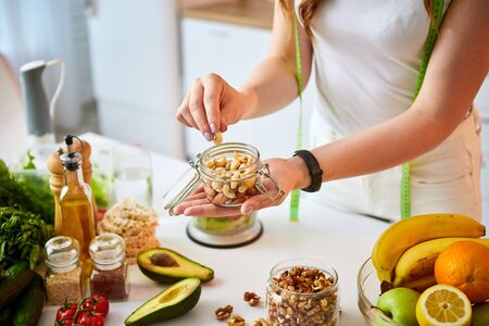 Young happy woman eating different nuts (cashew, hazelnut, almond) in modern kitchen. Healthy food and Dieting concept. Loosing Weightの写真素材