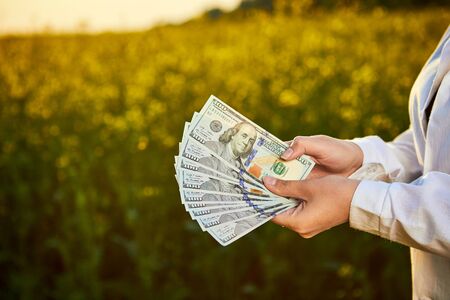 Agronomist woman or farmer holding money dollar banknote with blossoming cultivated canola field in...