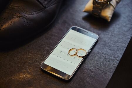 Wedding rings lie on the phone. Different accessories of businessman for creating style of  people on  wooden backgroundの写真素材