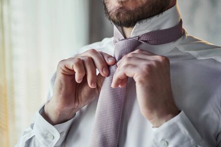 man in shirt dressing up and adjusting tie on neck at home. Men Fashionの写真素材