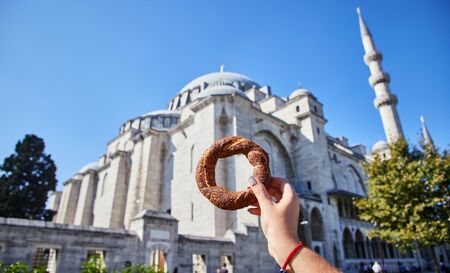 Simitci- a traditional Turkish round bagel with sesame seeds in hand on the background of a mosque in Istanbulの写真素材