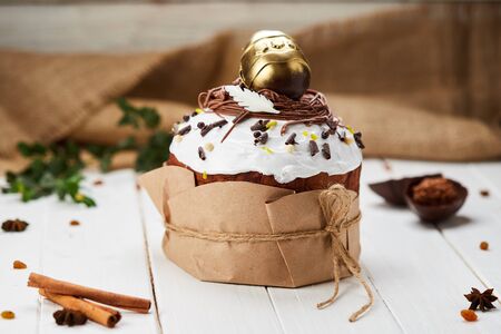 Easter cake decorated by golden chocolate egg on white wooden background, Traditional Kulich, Paska ...