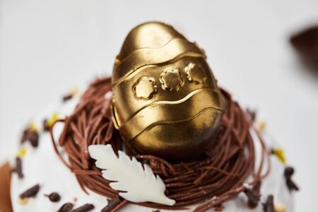 Easter cake decorated by golden chocolate egg on white wooden background, Traditional Kulich, Paska ...