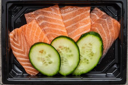 Fresh sliced salmon fillet with cucumber in plastic box ready for delivery. Wild atlantic fishの写真素材