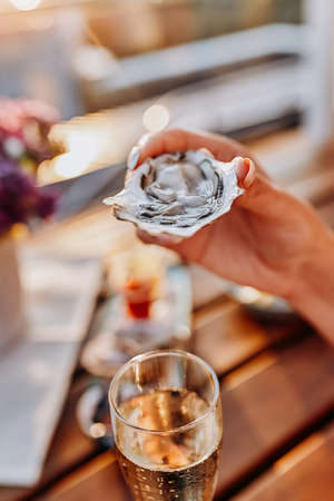 Woman eating fresh oysters and drinking chilled prosecco wine on the summer sunset. Seafood delicaciesの写真素材