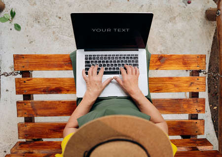 Senior woman gardener in a hat is watching something on a laptop computer and making a video call in...