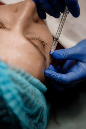 A cosmetologist injects a syringe into a patient, Botox