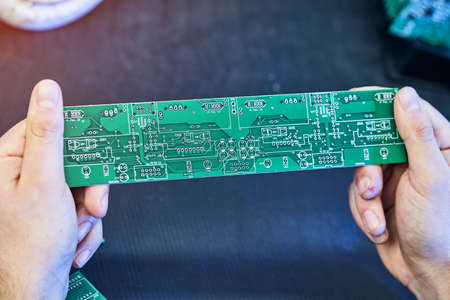 Green system board with microchips and transistors. Engineer factory worker electronics works with a...