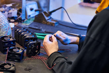 A master technologist makes fans for a computer cooling system. Computer Fan Parts lie on the table.