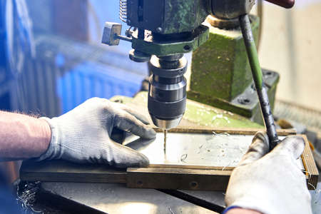 Employee drilling aluminium flat steel plate with bench drill. Metal Drill bit makes holes in Steel...