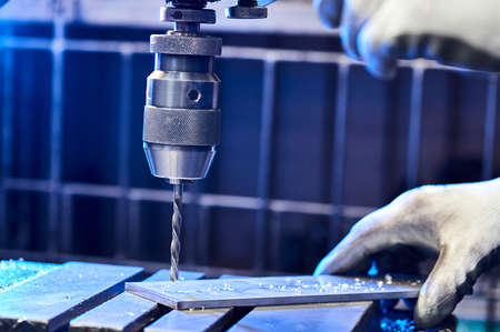 Employee drilling aluminium flat steel plate with bench drill. Metal Drill bit makes holes in Steel...