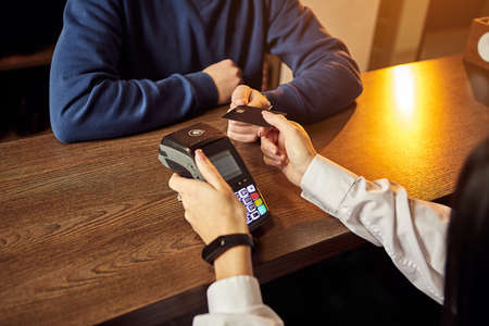 The customer's hand pays for a contactless credit card with NFC technology. Bartender with a Credit Card reader. Focus on hands.の写真素材
