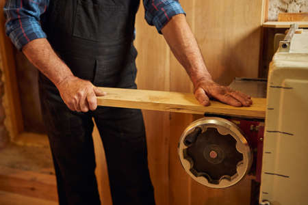 Senior carpenter in uniform works with a wood on a woodworking machine at the carpentry...