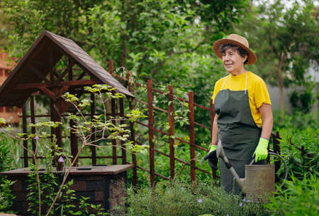 Senior woman gardener in a hat working in her yard with work tools. The concept of gardening,...