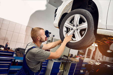 Auto mechanic checking running gear of automobile on service station. Male worker fixing problem...