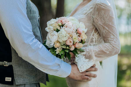 Groom holding a wedding bouquet in the hands standing near brideの写真素材