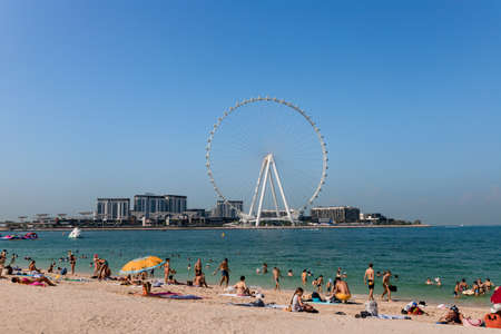 Dubai, UAE, November 2021, Panoramic view from JBR Beach over water towards Bluewaters Island with the Ain Dubai, the tallest and biggest observation or Ferris wheel in the world; people on beachのeditorial素材