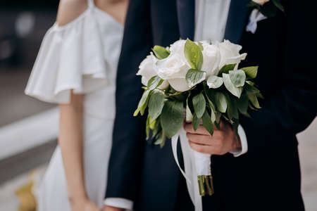 Groom holding a wedding bouquet in the hands standing near brideの写真素材