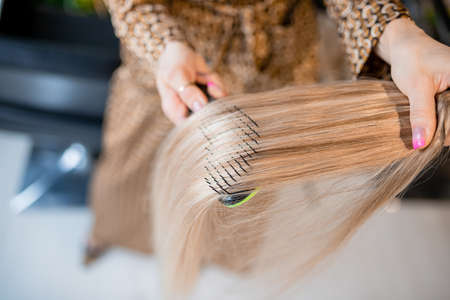 Professional hairdresser prepares blonde hair for extensions and combs them in a beauty salonの写真素材