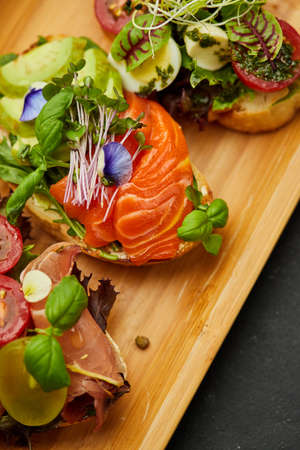 Assorted bruschetta set with salmon, parma and pesto souce. Italian antipasti snacks. Variety mix of small sandwiches on dark background. Photo for restaurant menuの写真素材