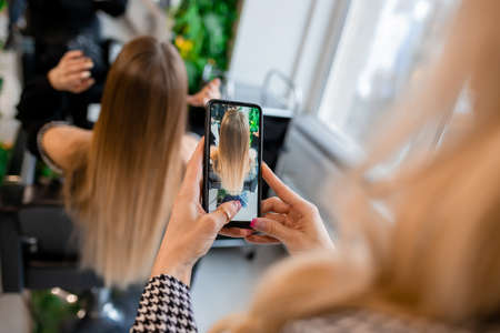 Professional hairdresser taking photo of blonde client's hair extensions for social media showcaseの写真素材