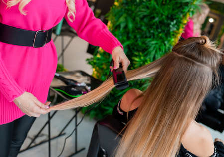 Professional hairdresser prepares blond hair for extensions and straightens them in a beauty salonの写真素材