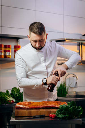 Portrait of handsome chef cooking raw meat in the kitchen. Cook salt and pepper the steak. Concept of Cooking process and preparing dishes.の写真素材