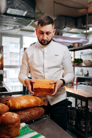 Handsome baker in uniform holding freshly baked bread at the bakeryの写真素材