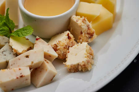 Cheese plate: Parmesan, cheddar, gouda, mozzarella and other with honey on white plate on dark...