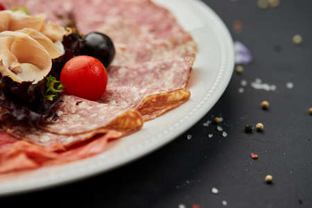 Cold meat platter, ham, sausage, salami, parma, prosciutto, bacon on cutting board with herb and olives over dark background. Meat appetizer, set of wine, close upの写真素材