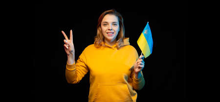 Ukraine national flag. Beautiful ukrainian girl with government flag on a stick in her hands on black background. Symbol of Ukrainian statehoodの写真素材