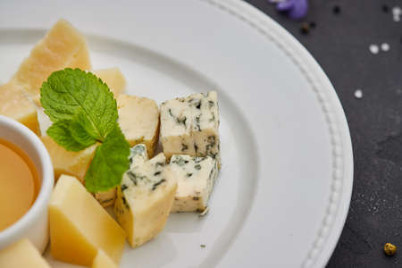 Cheese plate: Parmesan, cheddar, gouda, mozzarella and other with honey on white plate on dark...