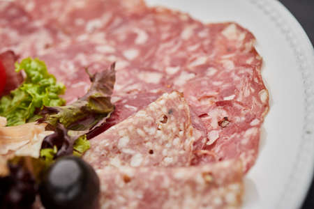 Cold meat platter, ham, sausage, salami, parma, prosciutto, bacon on cutting board with herb and...