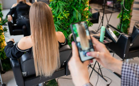 Professional hairdresser taking photo of blonde client's hair extensions for social media showcaseの写真素材