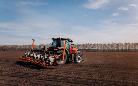 Spring sowing season. Farmer with a tractor sows corn seeds on his field. Planting corn with trailed...
